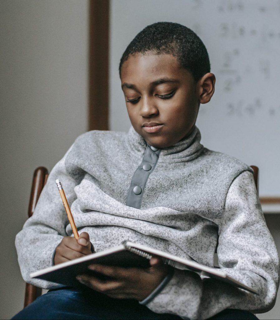 Boy sitting in a chair writing in a notebook. 